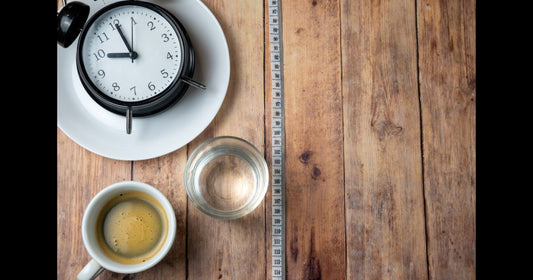 Black coffee and water next to a clock representing intermittent fasting and no-calorie drinks